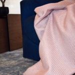 foto ambiente frazada Cavalari rosa puesta sobre sofá azul en espacio minimalista. All Star muebles