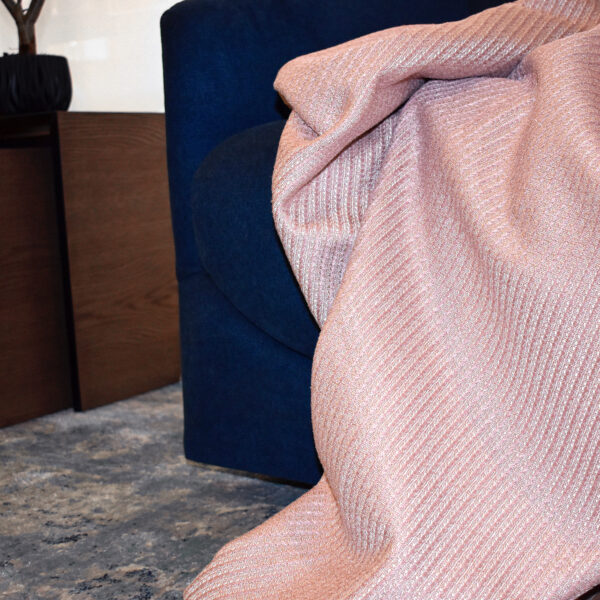 foto ambiente frazada Cavalari rosa puesta sobre sofá azul en espacio minimalista. All Star muebles