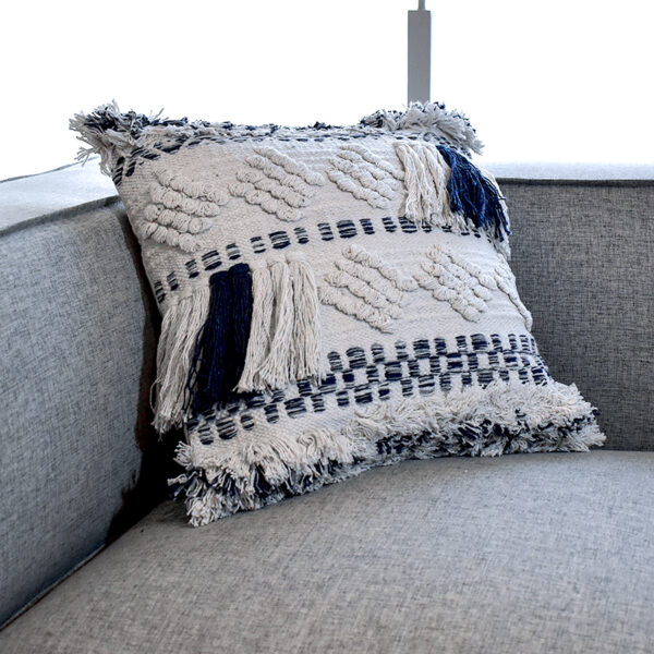 Funda con cojín cuadrada Antología color blanco y azul con tejido artesanal decorativo, ubicada sobre sofá gris, foto plano detalle. All Star muebles