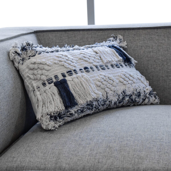 Funda con cojín rectangular Antología color blanco y azul con tejido artesanal decorativo, ubicada sobre sofá gris, foto plano detalle. All Star muebles