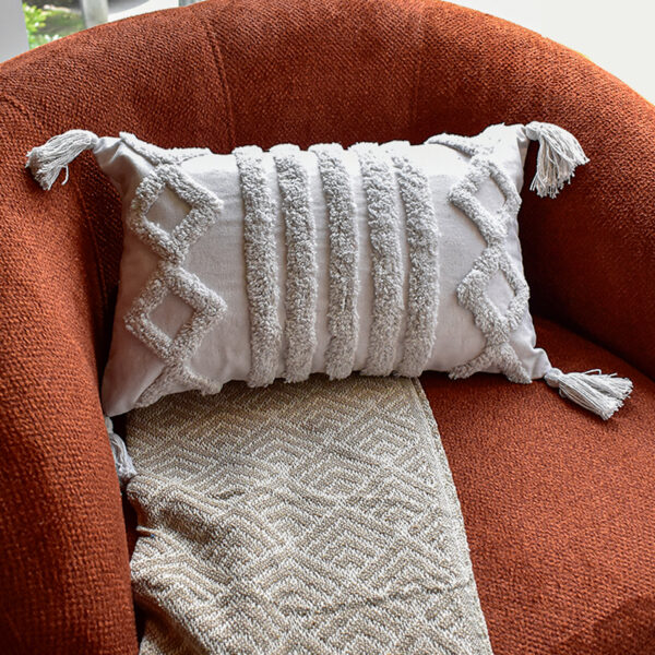 Funda con cojín rectangular Rustic color blanco con textura afelpada, ubicada sobre sofá rojo con una manta blanca complementaria, foto plano americano. All Star muebles