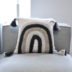 Funda con cojín Rustic multicolor con textura afelpada, ubicada sobre sofá gris en ambiente minimalista, foto plano americano. All Star muebles