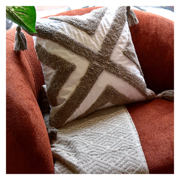 Funda con cojín Rustic color blanco con detalles moka y textura afelpada, ubicada sobre sofá rojo con una manta blanca complementaria, foto plano americano. All Star muebles