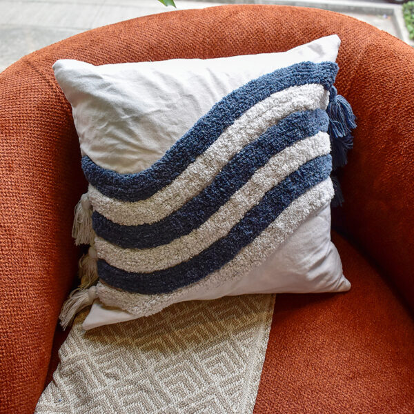 Funda con cojín Rustic color blanco con detalles azules y textura afelpada, ubicada sobre sofá rojo con una manta blanca complementaria, foto plano americano. All Star muebles