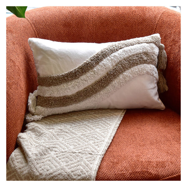 Funda con cojín rectangular Rustic color blanco con detalles avellana y textura afelpada, ubicada sobre sofá rojo con una manta blanca complementaria, foto plano americano. All Star muebles