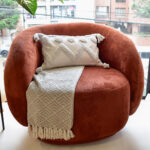 Funda con cojín rectangular Rustic color blanco con textura afelpada, ubicada sobre sofá rojo con una manta blanca complementaria, foto plano americano. All Star muebles