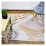 Ambiente de sala minimalista moderno con mesa auxiliar en madera, silla tapizada gris con patas en madera y tapete plateado y naranja con textura geométrica. All Star decoración