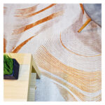 Fotografía plano detalle de tapete geométrico orgánico en tonos grises con naranja, con una silla de patas en madera encima. All Star decoración.