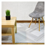 Ambiente de sala minimalista moderno con mesa auxiliar en madera, silla tapizada gris con patas en madera y tapete plateado con textura geométrica. All Star decoración