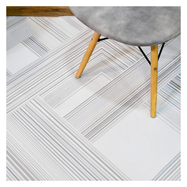 Fotografía plano detalle de tapete geométrico lineal en tonos grises con plateado, con una silla de patas en madera encima. All Star decoración.
