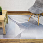 Ambiente de sala minimalista moderno con mesa auxiliar en madera, silla tapizada gris con patas en madera y tapete plateado y azul con textura geométrica. All Star decoración