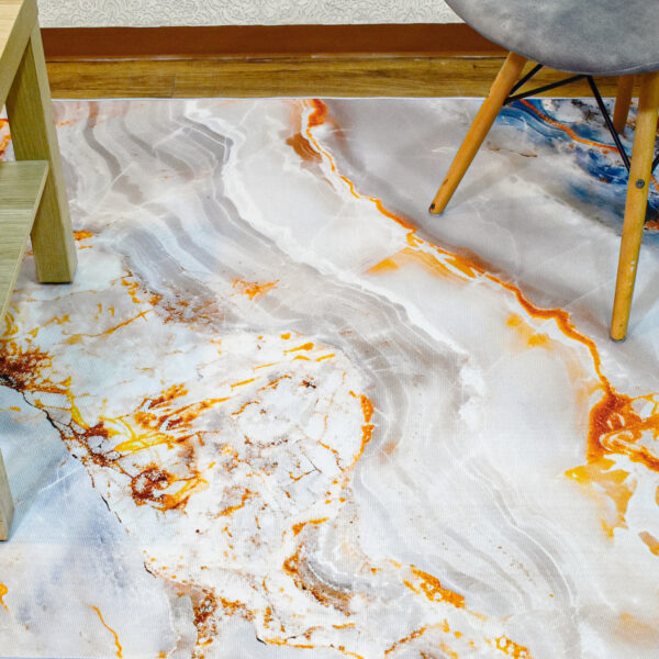 Fotografía plano detalle de tapete con textura mármol en tonos grises con plateado y naranja, con una silla de patas en madera encima. All Star decoración.