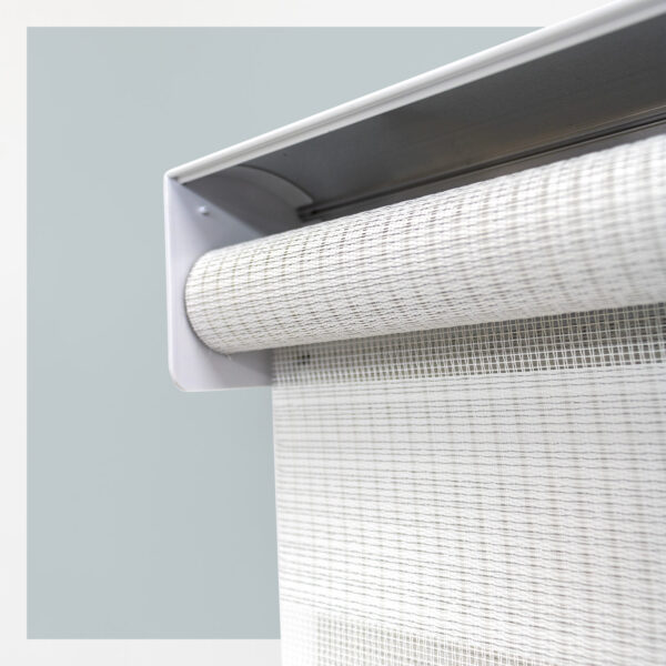 Detalle del mecanismo de una persiana enrollable tipo zebra con cadena plástica blanca y soporte lateral, textura de tela. All Star decoración