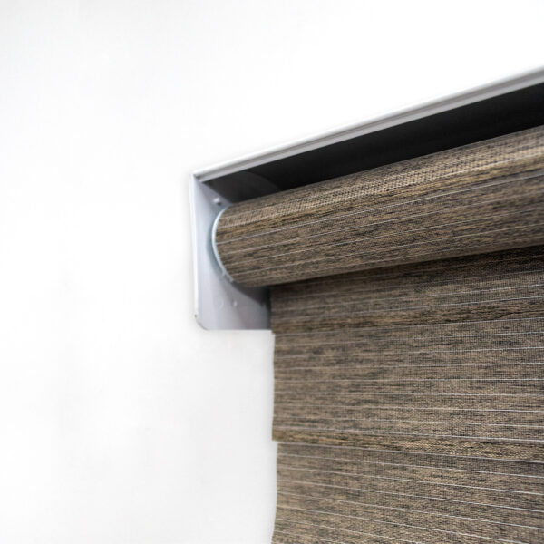 Detalle del mecanismo de una persiana enrollable tipo zebra con cadena plástica blanca y soporte lateral, textura de tela. All Star decoración