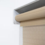 Detalle del mecanismo de una persiana enrollable tipo zebra con cadena plástica blanca y soporte lateral, textura de tela. All Star decoración