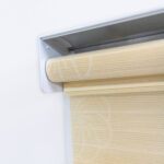 Detalle del mecanismo de una persiana enrollable tipo zebra con cadena plástica blanca y soporte lateral, textura en tela de flores. All Star decoración