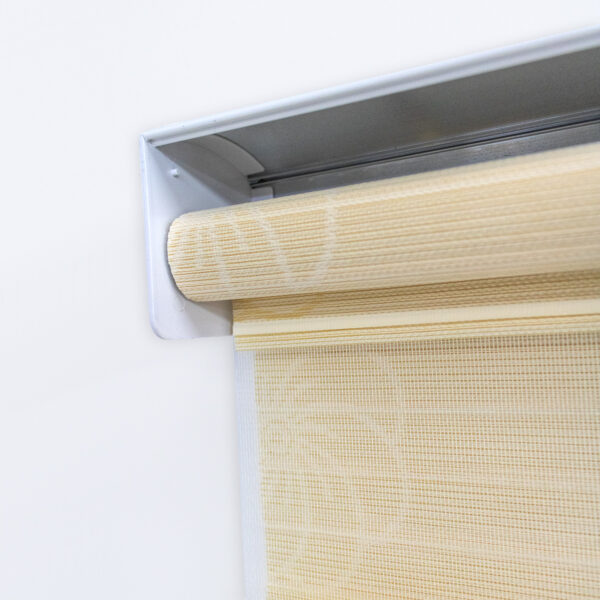 Detalle del mecanismo de una persiana enrollable tipo zebra con cadena plástica blanca y soporte lateral, textura en tela de flores. All Star decoración