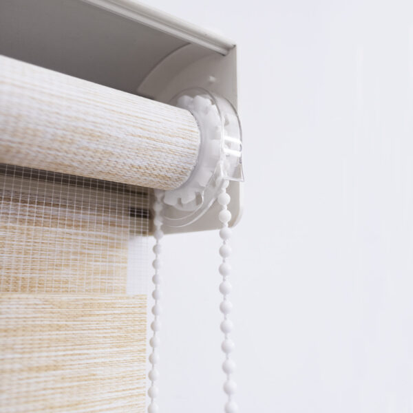 Detalle del mecanismo de una persiana enrollable tipo zebra con cadena plástica blanca y soporte lateral. All Star decoración