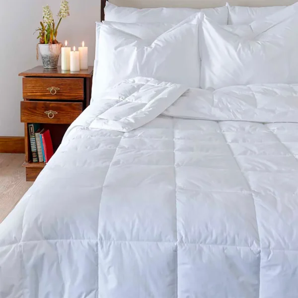 Edredón blanco acolchado puesto sobre cama en ambiente acogedor moderno visto de frente a plano medio. Muebles All Star