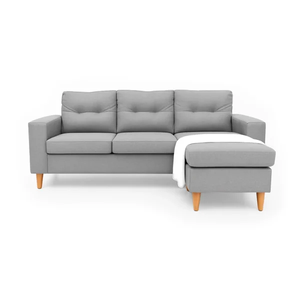 Sala en L Cielo con puff intercambiable tapizada en color gris, capitoneado en espaldar, con manta decorativa color blanca y patas en madera tono natural torneadas vista de frente. Muebles All Star